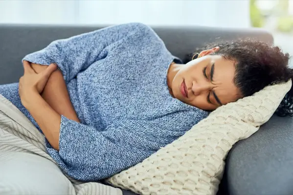 Woman experiencing stomach pain on the sofa at home