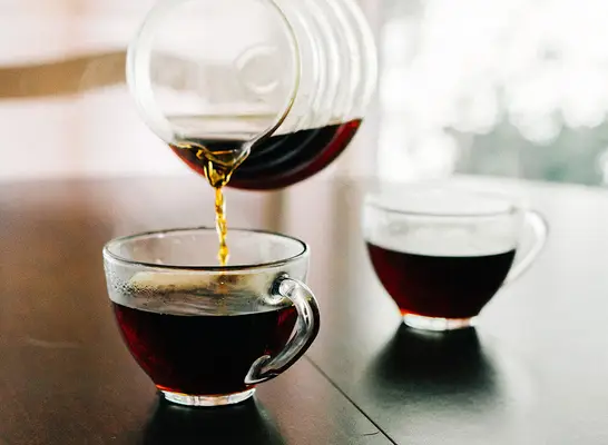 Cup of pour over coffee being poured into a mug in the morning.