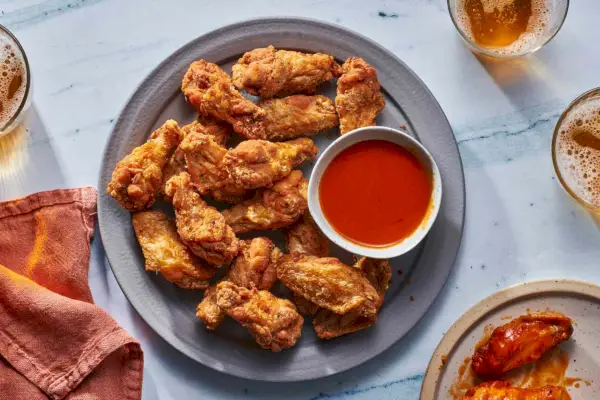 Un plato de alitas de pollo fritas crujientes servidas con salsa búfalo y vasos de cerveza