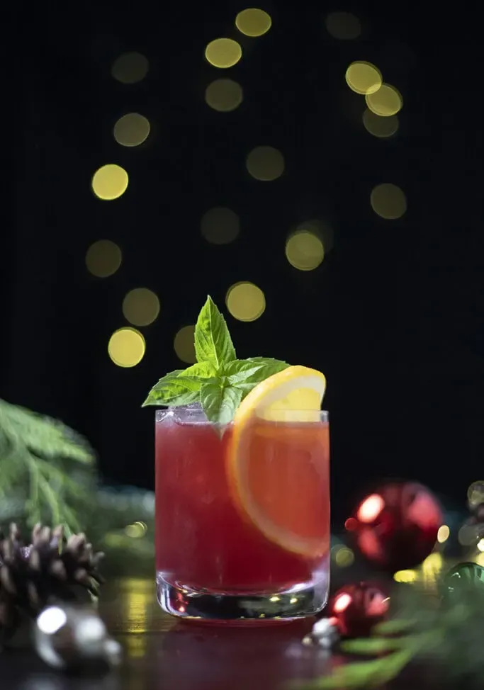 クリスマスの飾りと松ぼっくりの隣にローボールグラスに入った赤い飲み物。' loading='lazy' title=