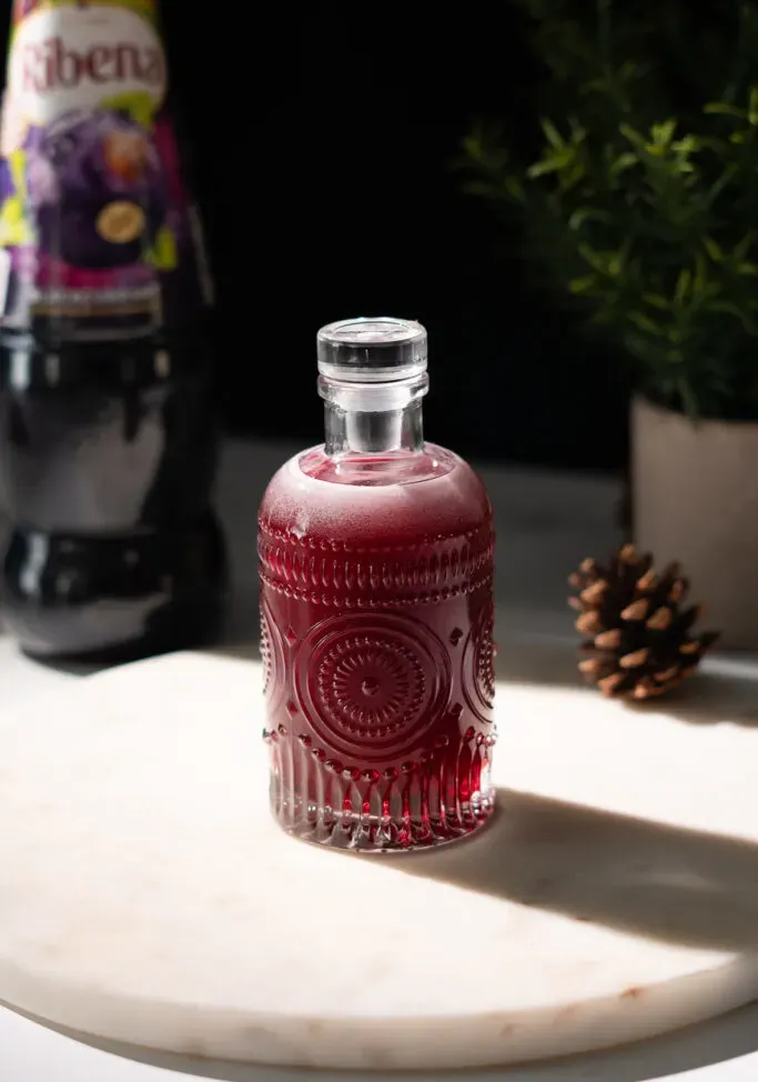 piccola bottiglia di vetro riempita con liquido rosso scuro su marmo bianco' title=