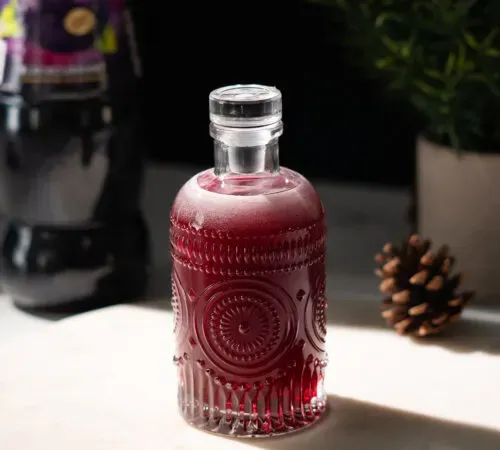 piccola bottiglia di vetro riempita con liquido rosso scuro su marmo bianco' title=