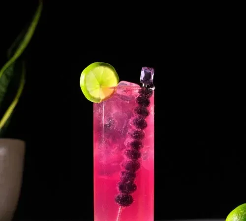 ein leuchtend rosafarbener Highball-Cocktail mit Limettenscheibe' title=