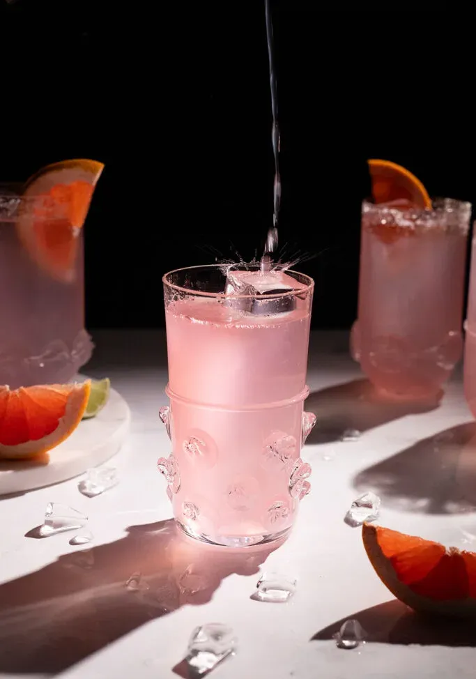 Rosa Flüssigkeit spritzt auf einen großen Eiswürfel in einem hohen Glas.' title=