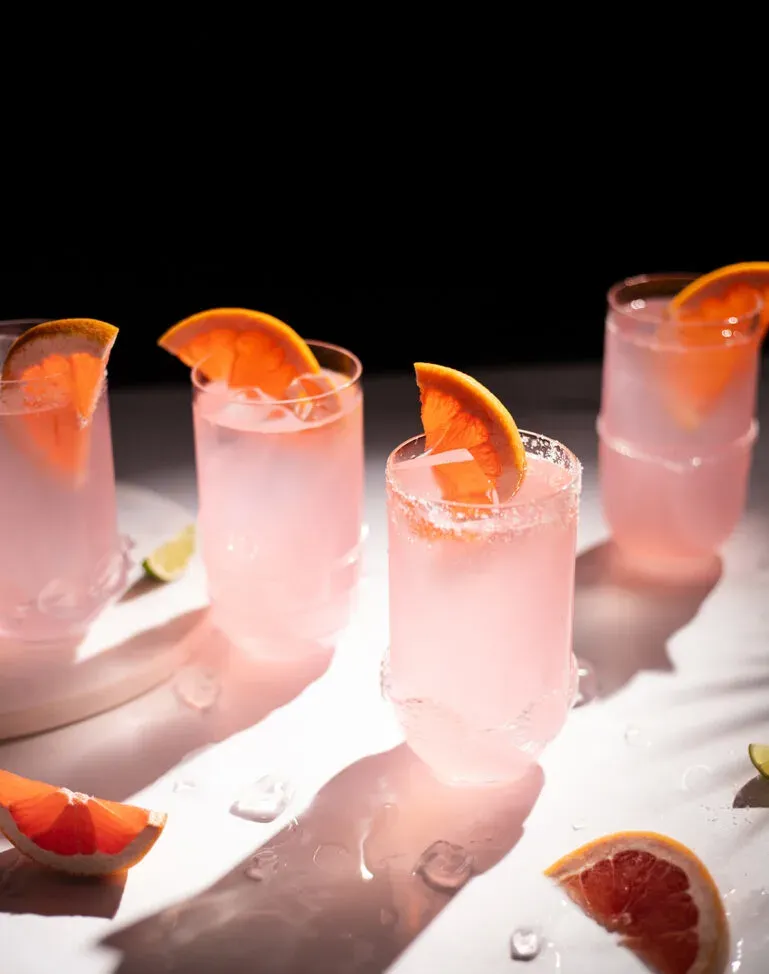 Vier Highball-Gläser gefüllt mit Eis und rosafarbener Flüssigkeit bei strahlendem Sonnenschein.' title=