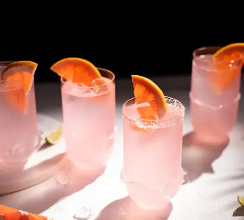 Vier Highball-Gläser gefüllt mit Eis und rosafarbener Flüssigkeit bei strahlendem Sonnenschein.' title=