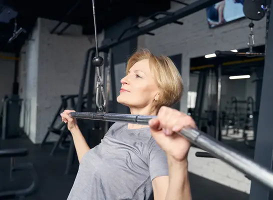 mature woman doing lat pulldown in gym to build muscle density and boost strength