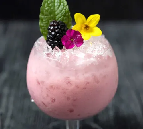 primo piano di un cocktail rosa al latte in un bicchiere da brandy con frutti di bosco e menta.' title=