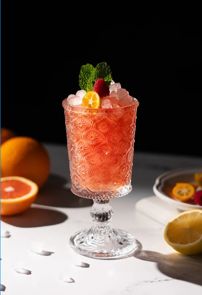 cóctel rojo en una copa con frambuesa kumquat y hojas de menta.' loading='lazy' title=