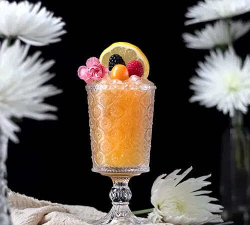 bebida de color naranja pálido en una copa de vidrio grabada con bayas encima.' title=