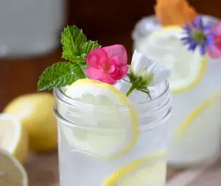 szklanki lemoniady z miętą i kwiatami.' title=