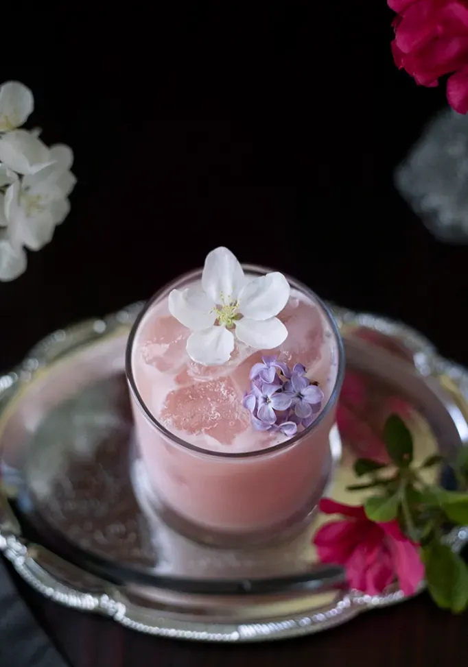 リンゴの花とライラックの花をあしらった淡いピンクの乳白色の飲み物を上から見た図' loading='lazy' title=