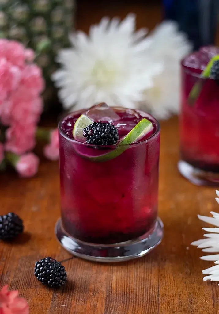 ブラックベリーとライムのスライスをトッピングした深い赤紫色のドリンク。' loading='lazy' title=