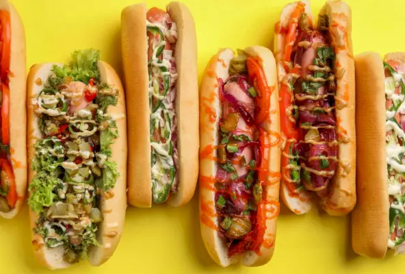 Deliciosos cachorros-quentes com diferentes coberturas em fundo amarelo