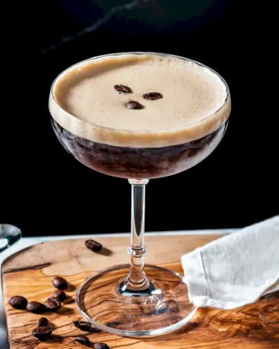 Oblíbené koktejlové espresso martini v koktejlové sklenici na stopce s ozdobou z kávových zrn.