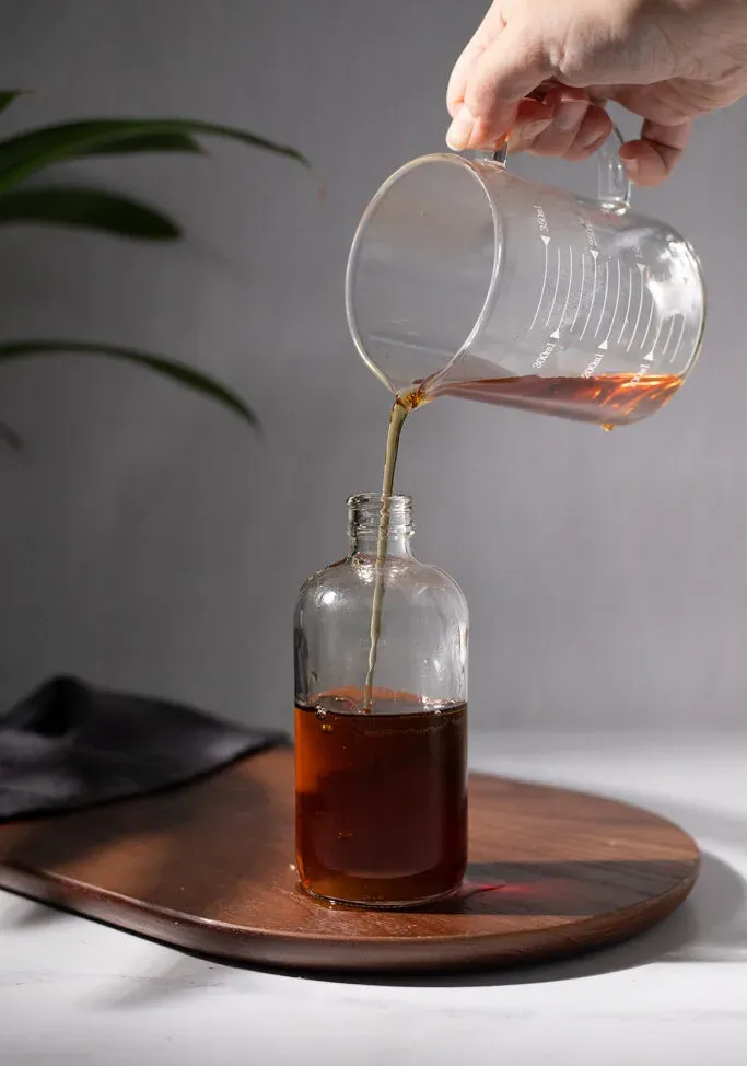 verter almíbar marrón de una taza medidora de vidrio en una botella.' loading='lazy' title=