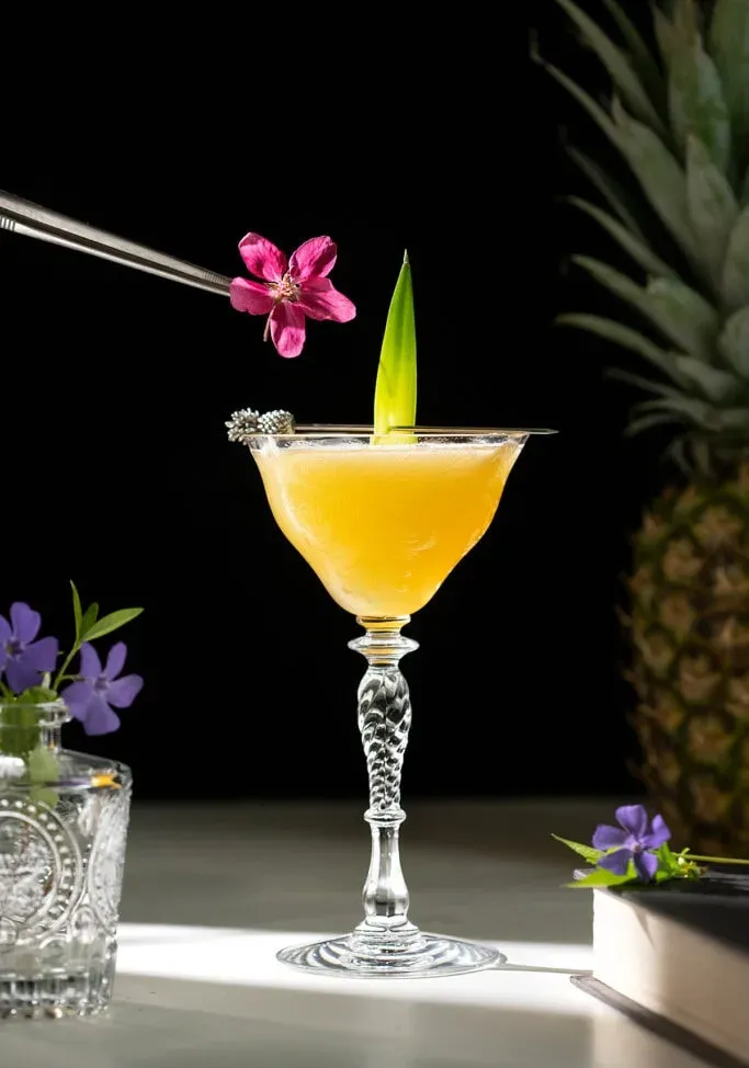 カクテルの上に食用の花を保持するトング。' loading='lazy' title=