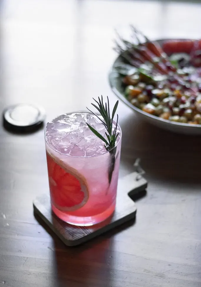 ein rosa Getränk, garniert mit Rosmarin, neben einer Schüssel Kichererbsen und gerösteten Karotten.' loading='lazy' title=