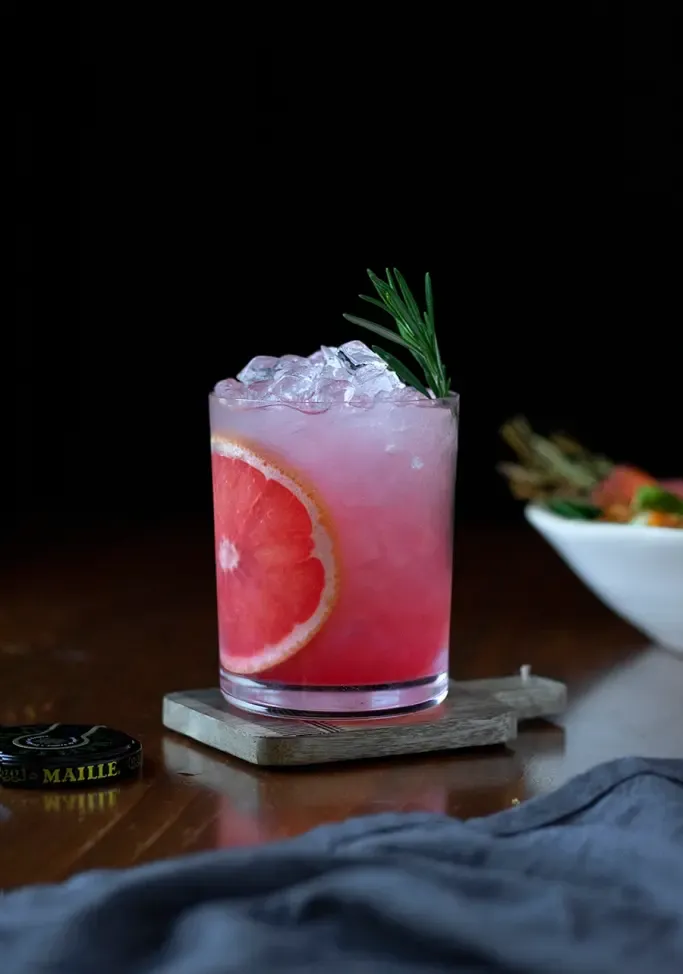 ein rosa Cocktail mit Crushed Ice und einem Grapefruitrad neben einer grauen Serviette.' loading='lazy' title=