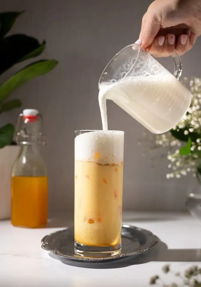 versando la schiuma di latte in un bicchiere di latte dorato ghiacciato.' loading='lazy' title=