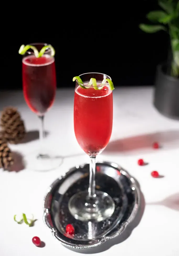 Rote Champagner-Cocktails, umgeben von Tannenzapfen und Preiselbeeren.' title=