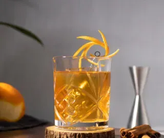 un elegante vaso bajo lleno de un cóctel dorado.' title=