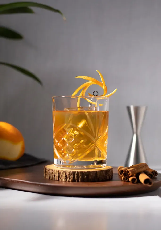 un elegante vaso bajo lleno de un cóctel dorado.' title=