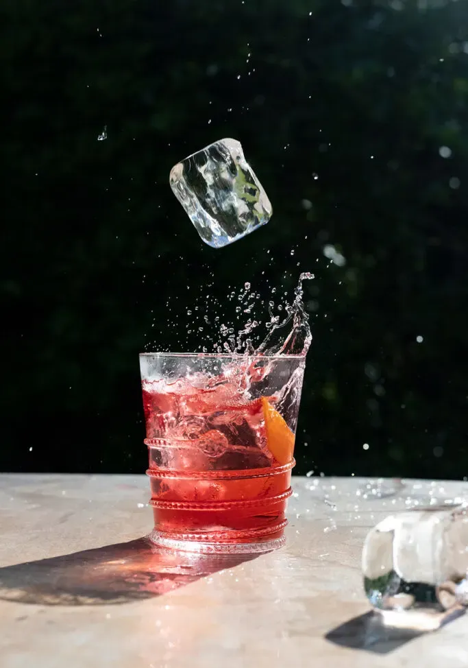 un gran cubo de hielo a punto de caer en una bebida roja en un vaso bajo.' title=