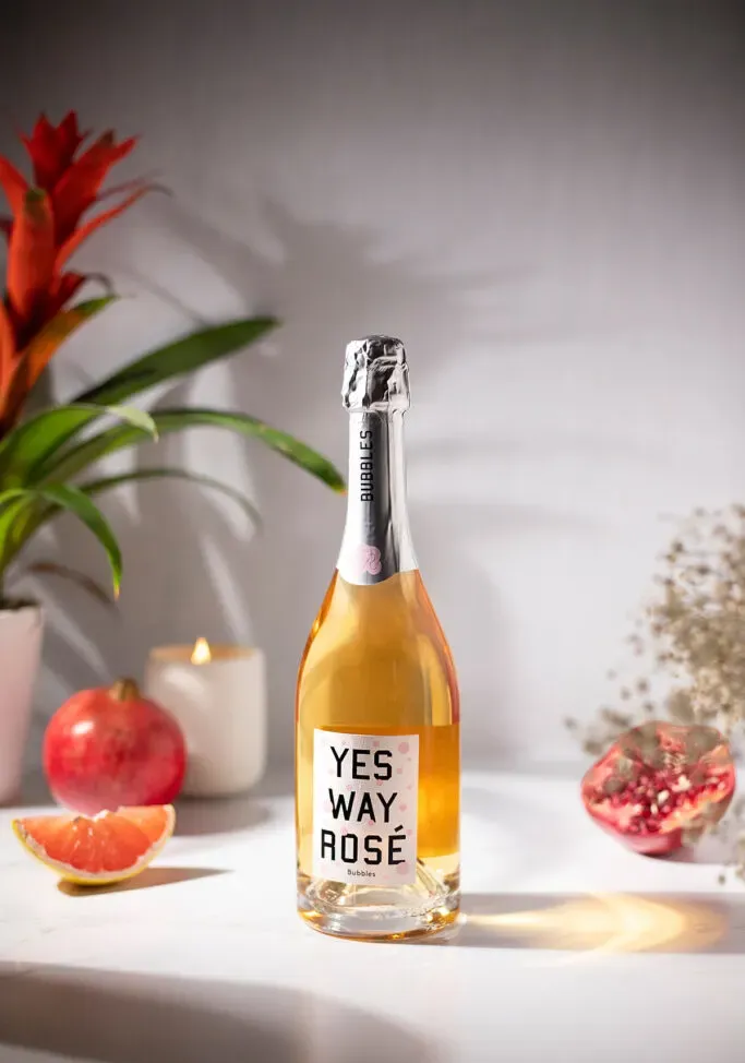 butelka Yes Way Rosé Bubbles obok granatów i roślin.' loading='lazy' title=