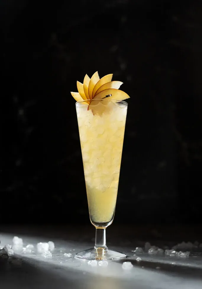 リンゴの扇子が添えられた背の高い黄色い飲み物。' title=