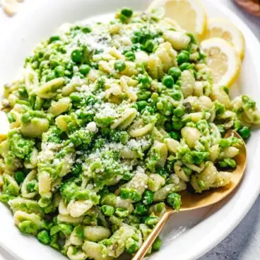 Macarrão com Ervilhas num prato com colher de servir e rodelas de limão.