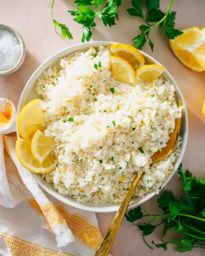 Recept na citrónovú ryžu v miske s lyžičkou, citrónmi a petržlenovou vňaťou.