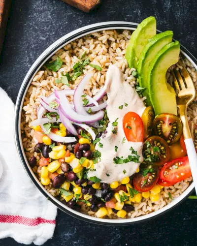 Burrito miska s čiernou fazuľou a kukuričným šalátom, avokádom, červenou cibuľou, paradajkami a ryžou.
