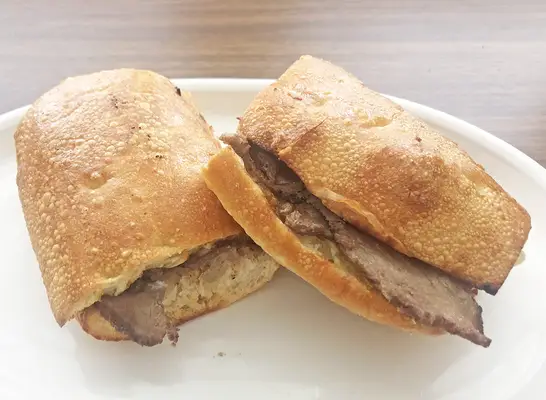 a panera cheesesteak sandwich cut in half on a white plate.
