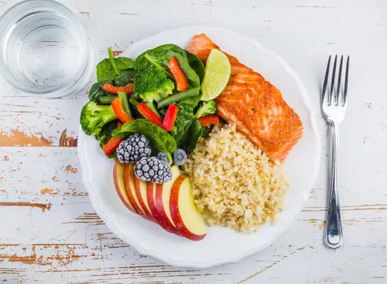 portioned plate with fish, grains, veggies, fruit, and a water glass
