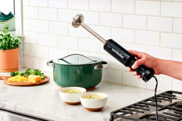 Osoba trzymająca Nutribullet Immersion Blender Deluxe Ustaw obok miski z zupą