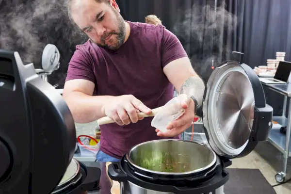 Pessoa raspando ingredientes com um utensílio de um recipiente na panela de pressão elétrica Instant Pot Duo 7 em 1, 6 quartos