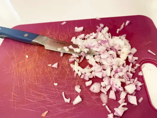 סכין חיתוך של Misen מוצג ליד בצל קצוץ על שולחן החיתוך