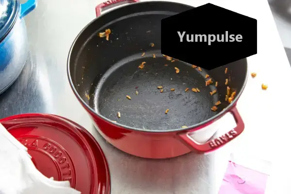 Niekoľko zrniek varenej ryže vo vnútri Staub 5,5-Quart Round Cocotte na kovovom pulte