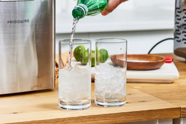 Una persona vierte agua en vasos de hielo fabricados con Frigidaire Countertop Nugget Ice Maker V2