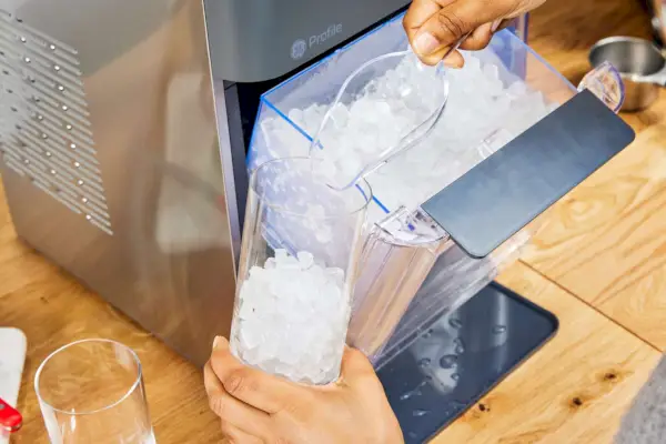 Una persona vierte en un vaso hielo elaborado con la máquina de hielo en pepitas para encimera GE Profile Opal 2.0 con tanque lateral