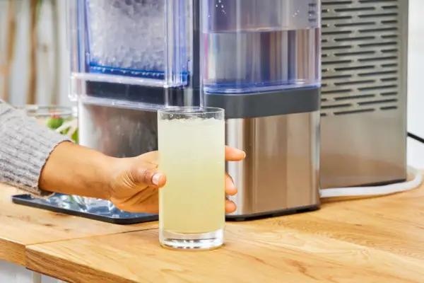 Una persona sostiene un vaso de líquido y hielo elaborado en la máquina de hielo en pepitas para encimera GE Profile Opal 2.0 con tanque lateral