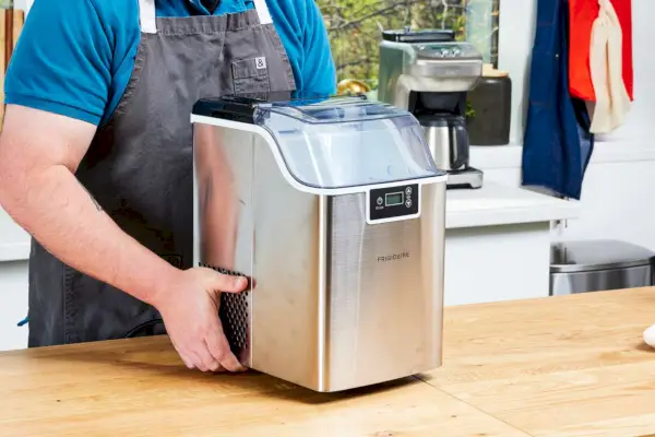 Una persona coloca la máquina de hielo Frigidaire Countertop Nugget Ice Maker V2 sobre una mesa