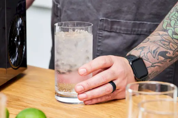 Una persona sostiene un vaso de agua y hielo elaborado en la máquina de hielo AGLucky Countertop Nugget Ice Maker