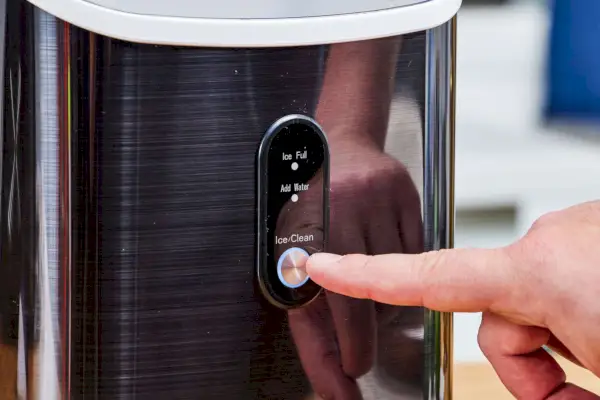 Una persona presiona el botón Hielo/Limpiar en la máquina de hielo AGLucky Countertop Nugget Ice Maker
