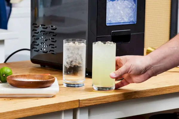 Una persona levanta un vaso de hielo elaborado con la máquina de hielo para encimera NewAir NIM044BS00 Nugget