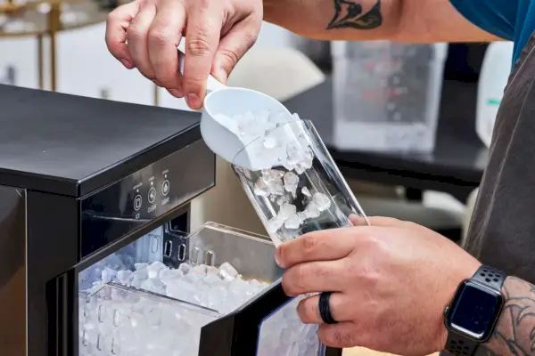 Una persona vierte hielo fabricado con la máquina de hielo para encimera NewAir NIM044BS00 Nugget en un vaso