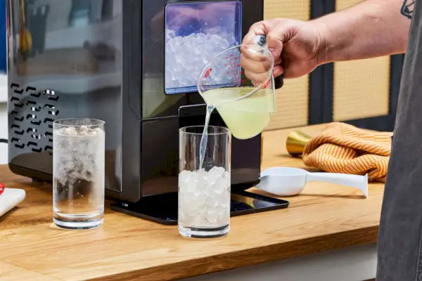 Una persona vierte líquido en un vaso de hielo elaborado con la máquina de hielo para encimera NewAir NIM044BS00 Nugget