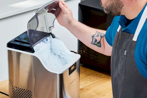 Una persona abre la parte superior de la máquina de hielo Frigidaire Countertop Nugget Ice Maker V2