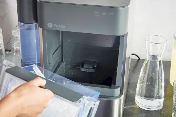 Persona que inserta un recipiente de agua dentro de la máquina de hielo en pepitas Ge Profile Opal 2.0